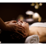 a woman laying in a dark room with candle lights receiving a facial treatment in tranquility.