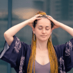 a woman with a long hair wearing a kimono sleeve boho outfit covering her head with both hands closed eyes and relaxed.