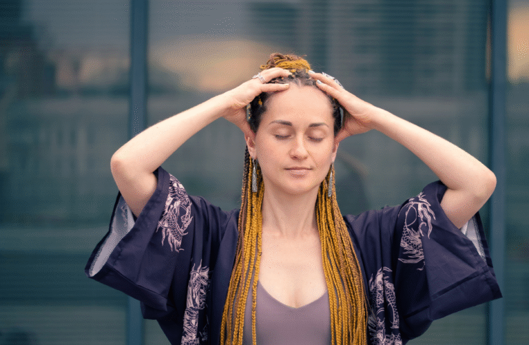 a woman with a long hair wearing a kimono sleeve boho outfit covering her head with both hands closed eyes and relaxed.